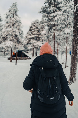 Woman in black coat walking towards snowy laavu in Rovaniemi, Laplandの写真素材