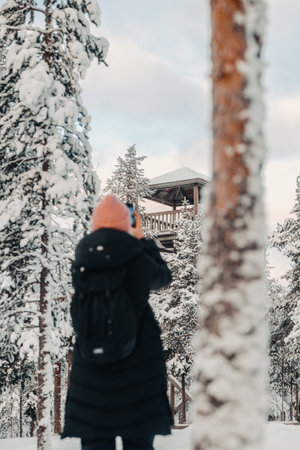 Woman taking photos of lookout tower in snowy forest in Rovaniemi, Laplandの写真素材
