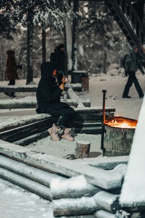 Woman sat next to fire at snowy laavu in winter in Rovaniemi, Laplandの写真素材