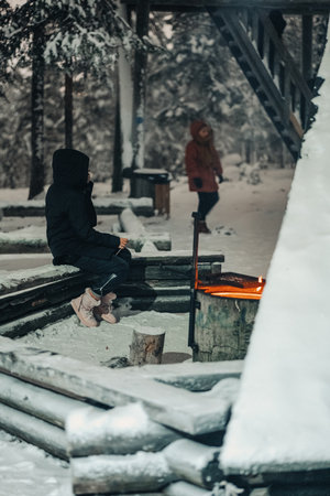Woman sat next to fire at snowy laavu in Rovaniemi, Lapland in winterの写真素材