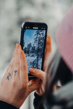 Woman with finger tattoos taking photos on phone in Rovaniemi, Lapland in winterの写真素材