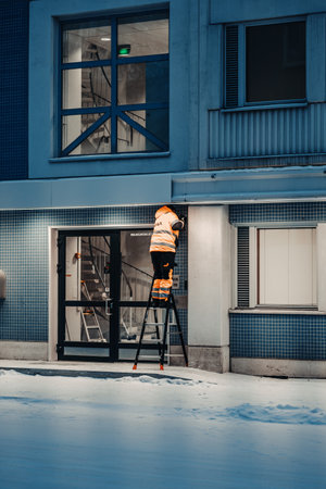 Worker in orange high vis on ladder in snow in Rovaniemi, Laplandの写真素材