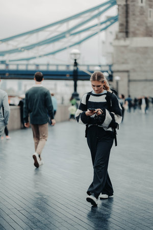 Girl on phone walking in front of Tower Bridge in London, UKの写真素材