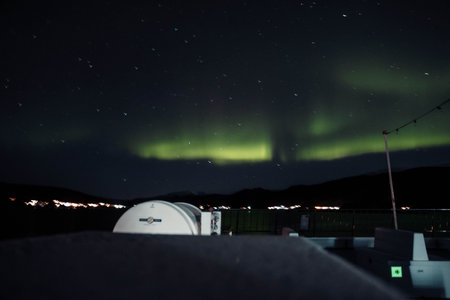 Strong aurora borealis in starry sky above cruise ship in Tromso, Norway