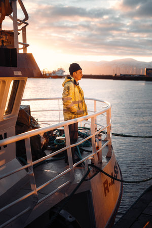 Fisherman stood on the front of boat in the arctic in Tromso harbour, Norwayの写真素材