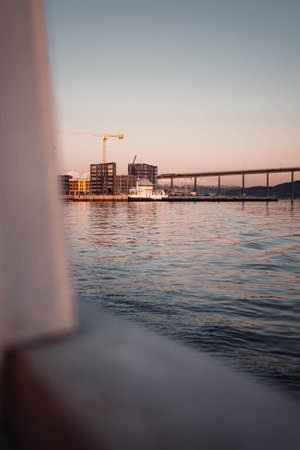 Tromso bridge behind buildings on skyline at sunset, shot from fjord in Norwayの写真素材