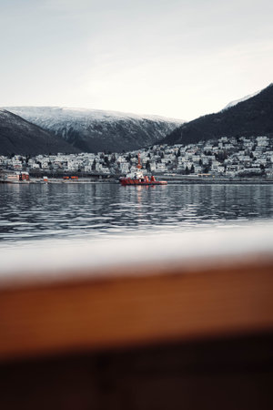 Boat on water outside Tromso harbour in front of snowy arctic mountains, Norwayの写真素材
