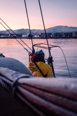 Man on deck of wooden fishing boat at sunset on fjord in Tromso, Norwayの写真素材
