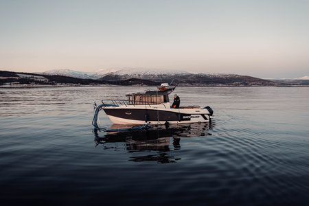 Small fishing boat at sunset on arctic fjord near mountains in Tromso, Norwayの写真素材