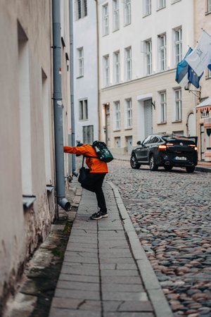 Man in orange coat leaning on building on old town street in Tallinn, Estoniaの写真素材