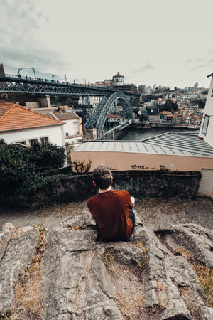 Man sat on rock with view of Ponte Dom Luis I bridge in Porto, Portugalの写真素材