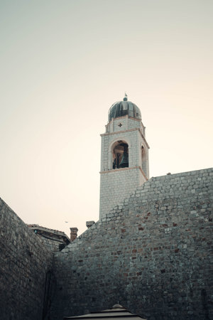 Church bell tower in golden hour sky above Dubrovnik old town city wall, Croatiaの写真素材