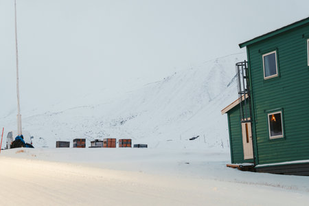 Snowy mountains behind green wooden building in Longyearbyen, Svalbardの写真素材