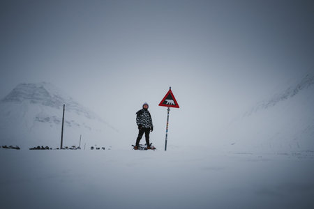 Man stood next to polar bear warning sign in Longyearbyen, Svalbard in the snow