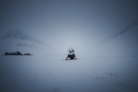 Snowmobile parked in snowy valley under clouds in Longyearbyen, Svalbardの写真素材
