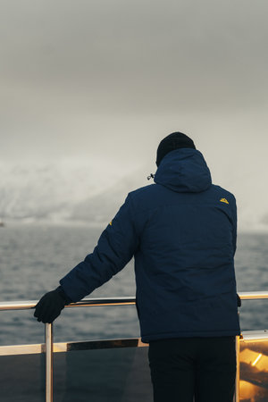 Man on tour boat in the arctic looking at snowy mountains, the Lyngen Alpsの写真素材