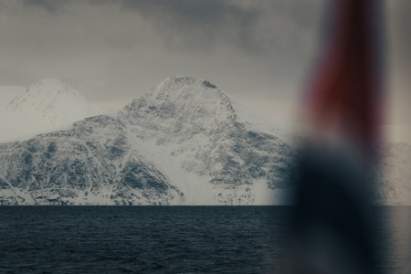 Snowy mountain behind Norwegian flag in the arctic Lyngen Alps in winterの写真素材