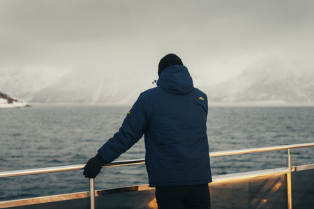 Man stood next to arctic tour boat railing looking at misty Lyngen Alpsの写真素材
