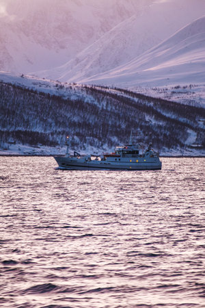 Fishing boat at sunset on the arctic ocean in winter in northern Norwayの写真素材