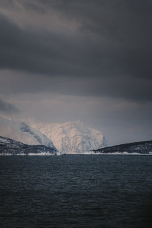 Snowy mountains under clouds in the distance by arctic ocean in northern Norwayの写真素材