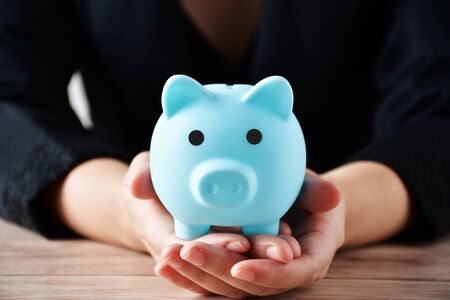 The woman's hand is carrying a piggy bank piggy bank in the hand placed on a wooden tableの写真素材