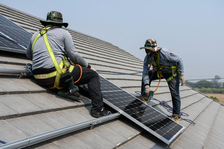 Workers are installing gray roof tiles wearing seat belts to ensure safe working at heights.