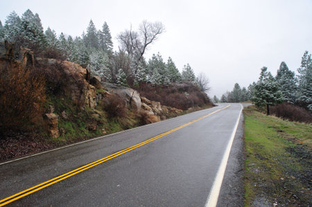 Sierra mountain road and yellow dividing line with trees and lite snow