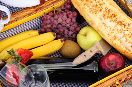 Closeup of the contents of a picnic backet these include red wine, grapes, red and green apples, kiwi fruit, bannas, strawberries amd a loaf of french breadの写真素材