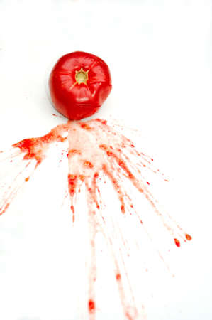 A single bright red tomato splattered on a white background with juice and seeds spread across the isolationの写真素材