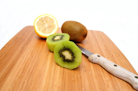 Kiwi fruit peeled and sliced in half with a lemon and knife on a bamboo cutting boardの写真素材
