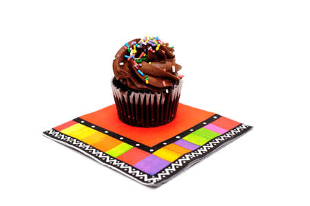 Single cupcake with chocolate frosting and colorful sprinkles on top of a brightly colored party napkin isolated on whiteの写真素材
