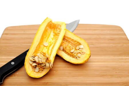 Delicata squash sliced in half exposing the many seeds inside on a bamboo cutting boardの写真素材