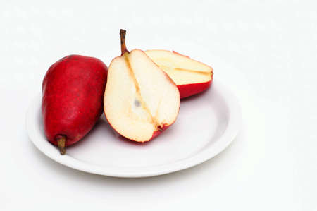 Red pears on a white saucer on pear is sliced in half showing the core and seedsの写真素材