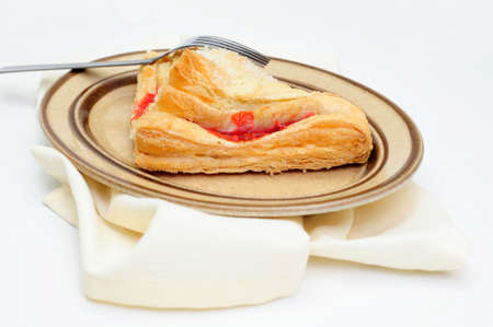A sweet Cherry Turnover with course ground sugar on top served on an oval brown colored saucer with a light colored cloth napkin under the plateの写真素材