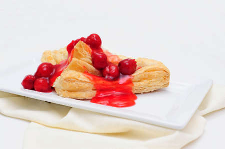 Cherry Turnover with a topping of cherries and a red cherry sauce served on a white rectangular saucer and a light colored napkinの写真素材