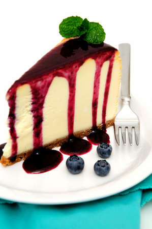 Plain Cheesecake with a Blueberry sauce poured over the top with fresh berries on the plate next to the cake and topped with a mint leaf.の写真素材