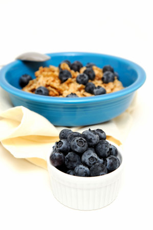 Bowl of cold breakfast cereal with fresh blueberries on a white background