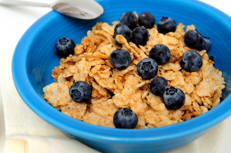 Bowl of cold breakfast cereal with fresh blueberries on a white background