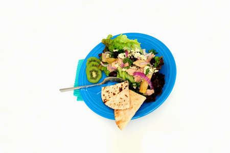 Tuna salad on a bed of Red Leaf Lettuce with Artichoke hearts, Kalamata olives, red onions and Feta Cheese, Kiwi slices and pita bread served on a turquoise colored plateの写真素材