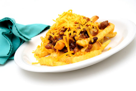 Melting cheddar cheese over the top of french fries covered in spicy chili with meat and beans