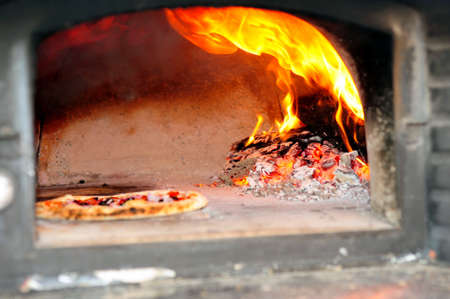 Baking Pizzas in a wood burning pizza oven with glowing coals and embers with flames  shooting upの写真素材
