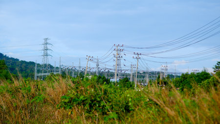 View of a high-voltage power substation located in the middle of a natural landscape. Steel transmission towers tower in the backgroundの写真素材