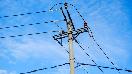 Photo of a concrete electric pole with wires stretching across a bright blue sky. The sturdy pole, with its orange insulators sticking outの写真素材