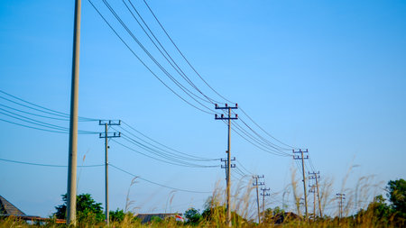 A series of electric poles and power lines stretching across the vast, clear blue sky. The poles stand tall on the horizon, carrying a network of cables that symbolize connectivityの写真素材