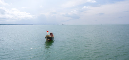 Landscape image of a traditional wooden fishing boat floating alone on a calm sea under a clear skyの写真素材
