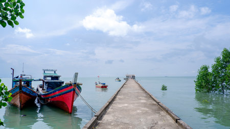A beautiful view of colorful traditional fishing boats moored near a concrete pier stretching out into the calm turquoise sea.の写真素材