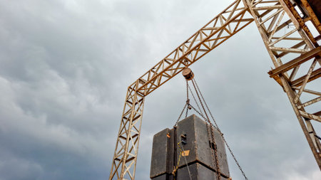 Heavy duty industrial crane lifting large concrete blocks under dramatic cloudy skiesの写真素材