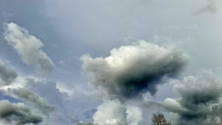 Dramatic and expansive view of a dynamic sky filled with large, textured clouds. The varying shades...