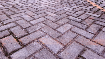 Low angle perspective shot of a gray cobblestone sidewalk with a herringbone pattern extending into...