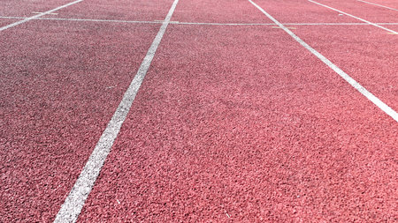 Close-up image of a red synthetic running track surface with clearly marked white lane linesの写真素材